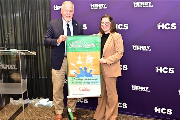 Principal Thomas and state superintendent Woods stand with banner.